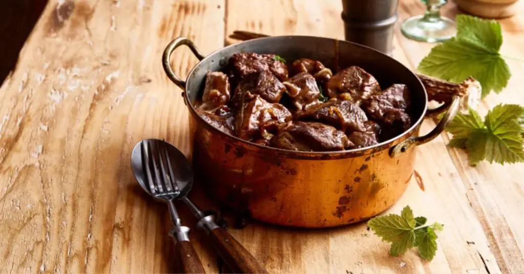 A casserole with wild boar stew, the meat has a muscular but tender appearance and is black-red in colour.