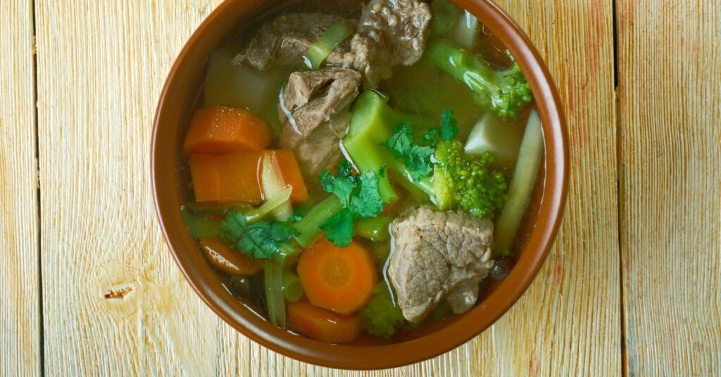 A bowl of a soup called Garmugia, with fava beans, peas, scallions, asparagus, ground beef, and chicken broth.