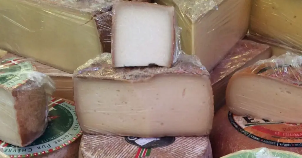 Some forms of Pecorino di Pienza cheese cut in half, the inside is light in color and semi-soft, the crust is dark, almost anthracite gray.