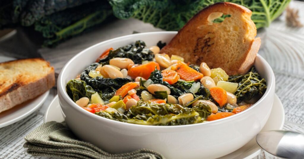 A bowl of Frantoiana soup, cooked with  carrots, potatoes, zucchini, celery, and kale, along with fresh borlotti beans.