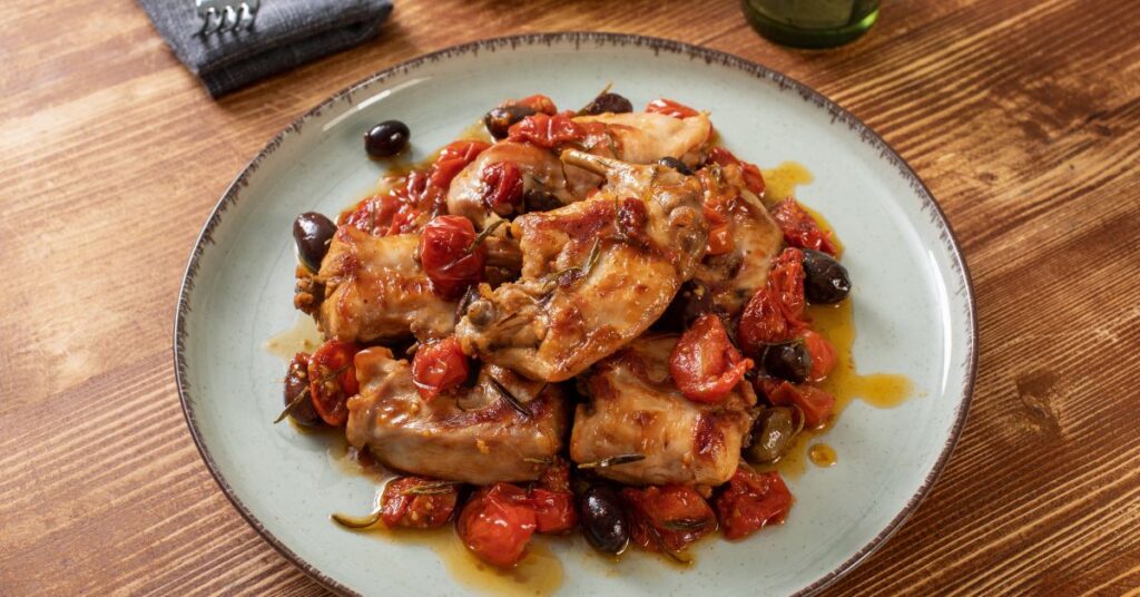 A plate of stewed rabbit with black olive and tomato.