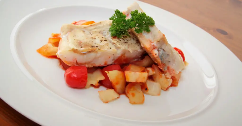 Dish with two fillets of Stockfish cooked to perfection placed on a bed of potatoes, all covered with a fresh tomato sauce.