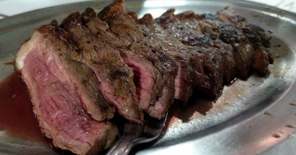 A silver plate with slices of steak cooked rare and pink internal meat and burnt brown cooked exterior on top.