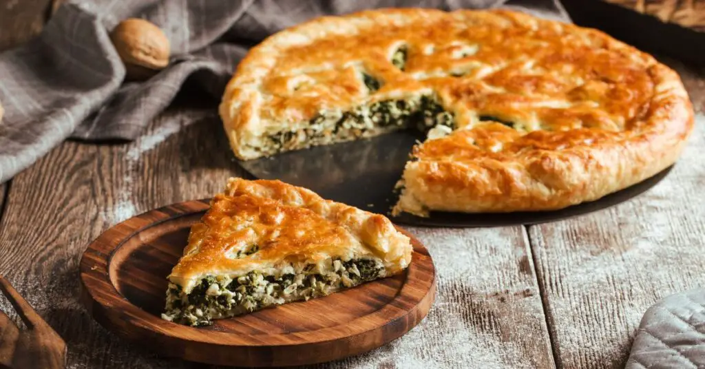 A savory tart, flat with a browned and crunchy exterior, filled with a green vegetable mix.