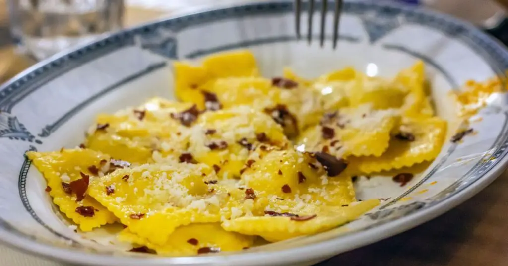 A plate of filled pasta, called tortelli with potato. Topped with pancetta (bacon) chunks.