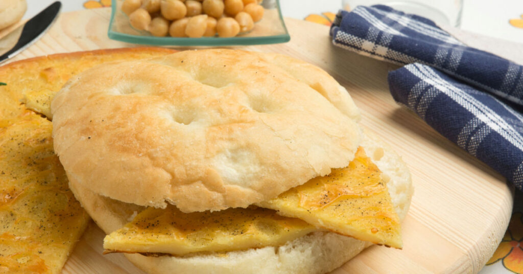 A white and soft rectangular sandwich, stuffed with a chickpea flour omelette, with a golden and creamy appearance.