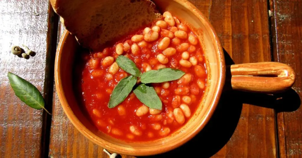 A terracotta bowl full of large white beans immersed in a bright red tomato sauce, this dish is called Fagioli all'Uccelletto