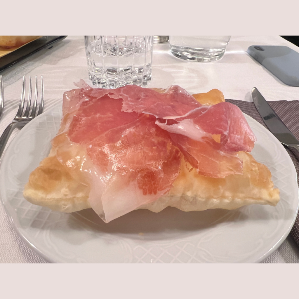 A ficattola, square of fried dough, golden, crunchy and swollen, with very thin slices of ham placed on top.