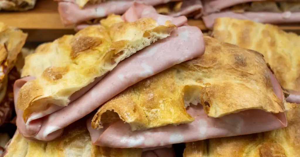 Rectangular focaccias, crunchy and golden on the outside and white and soft on the inside, contain thin slices of finely chopped Mortadella, which protrude from the sandwich.