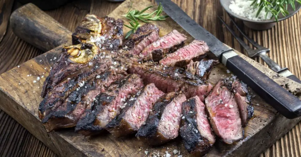 A Florentine steak sliced ​​and placed on a wooden cutting board. The meat is well done and crispy on the outside and pinkish and tender on the inside.