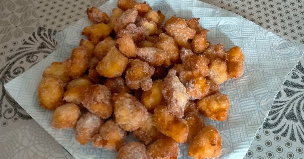 A plate with a pyramid of freshly fried rice pancakes, they are irregular balls with an amber color and covered with granulated sugar.