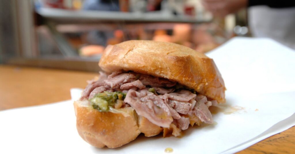 A sandwich with "lampredotto" seen up close, the very tender meat comes out of the loaf and you can also see the green sauce with which the sandwich is seasoned.