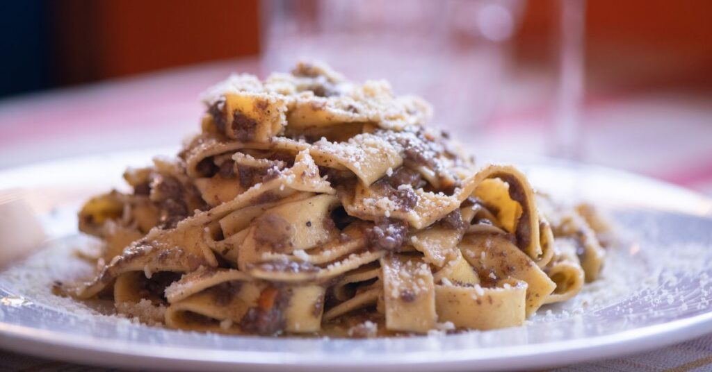 A plate full of pappardelle with boar ragu and grated parmesan on top.