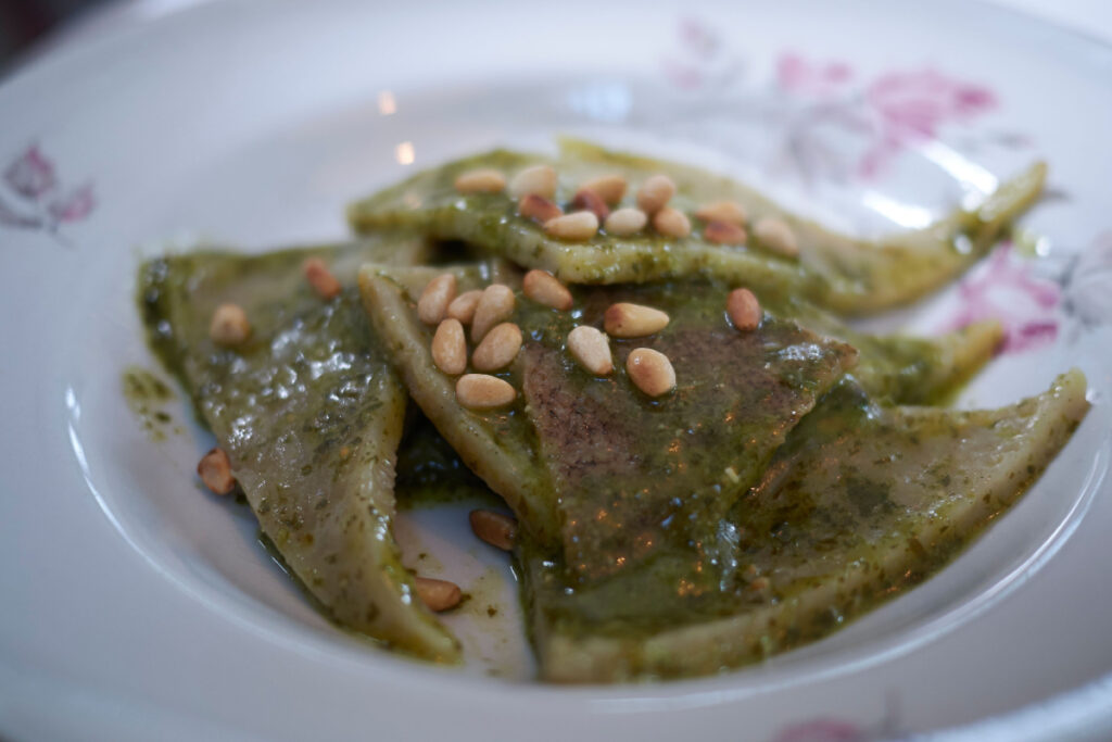 A plate of Testaroli, a rhombus-shaped pasta, seasoned with green pesto and some toasted pine nuts.