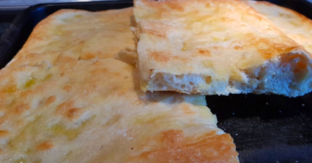 A piece of Tuscan flatbread cut in half, the outside is golden, greasy and crunchy, while the inside is soft, honeycombed and almost white in colour.