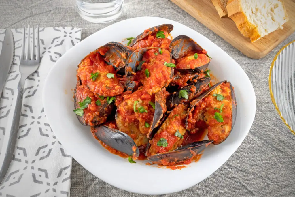 A plate of stuffed mussels, they are slightly open and stuffed with meat and completely enveloped in a tomato sauce.