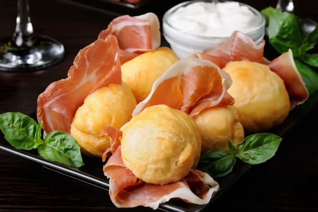 A group of coccoli, crunchy and golden balls of fried dough, flanked by finely sliced ​​ham and spreadable stracchino.