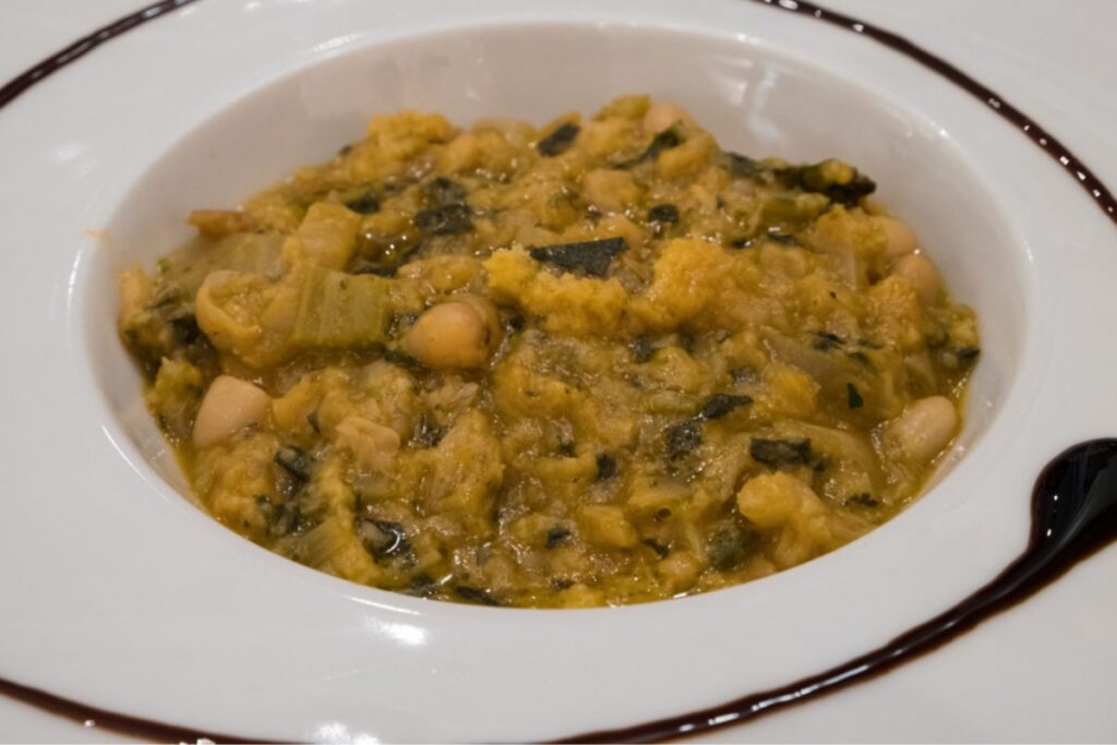 A plate of Tuscan soup, called Ribollita, made with stale bread, beans and various seasonal vegetables. It is very creamy and rustic in appearance.