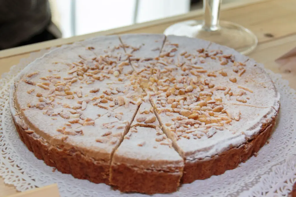 A Mantovana cake cut into slices, the crust is fragrant and browned, the top has a coating of icing sugar and lots of toasted pine nuts.