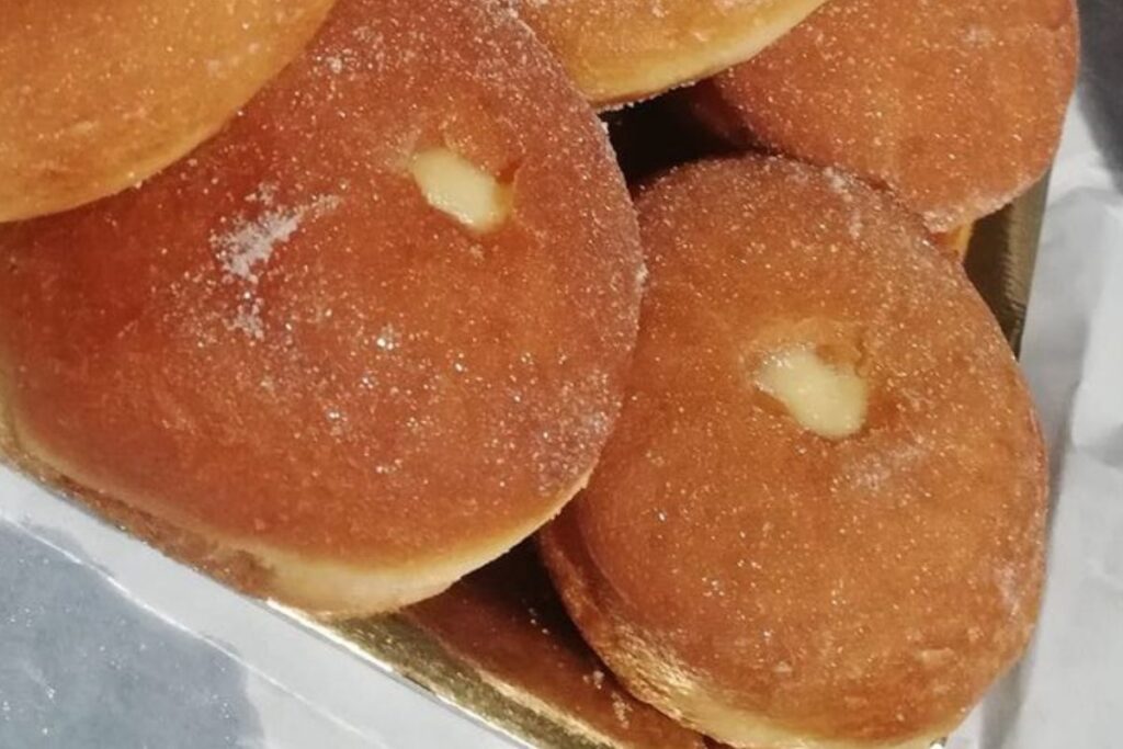 Two bomboloni from Tuscany, these sweet pastries are filled with cream and look swollen and covered in sugar. Precisely because of their swollen appearance they are called bomboloni, like a bomb.