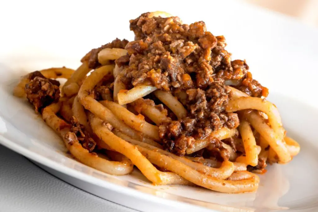 A plate of pici al ragu, a handmade pasta with an irregular and thick shape, served with a very thick and dense ragu sauce, with small pieces of minced meat.