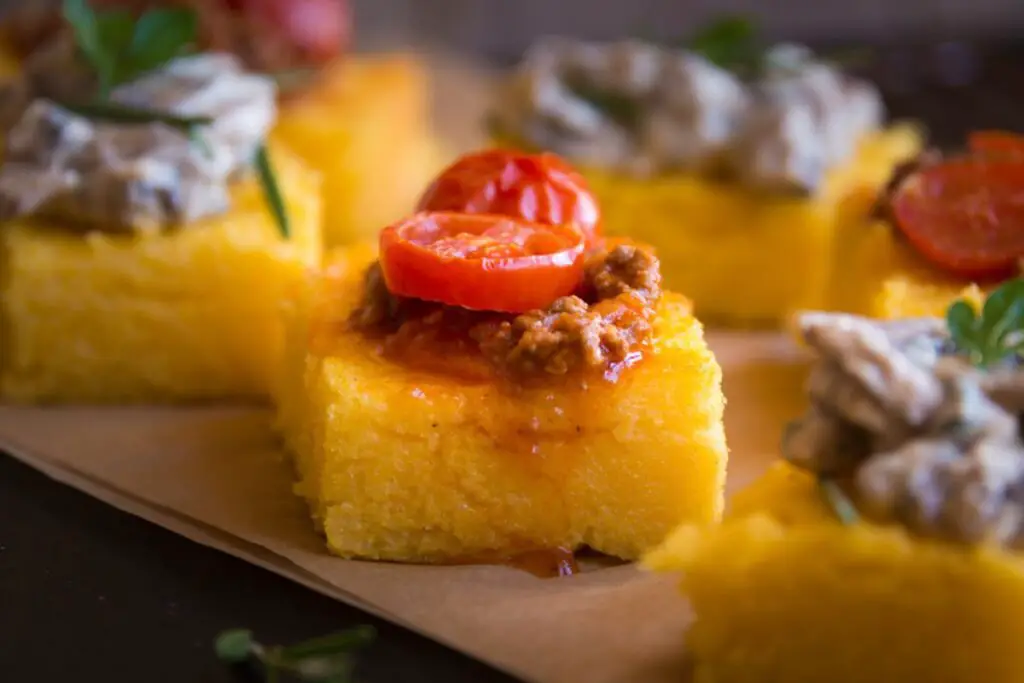 A thick slice of fried polenta with a golden color and a crunchy appearance. Chicken liver is spread over the polenta, exactly as you would do it on a toasted bread.