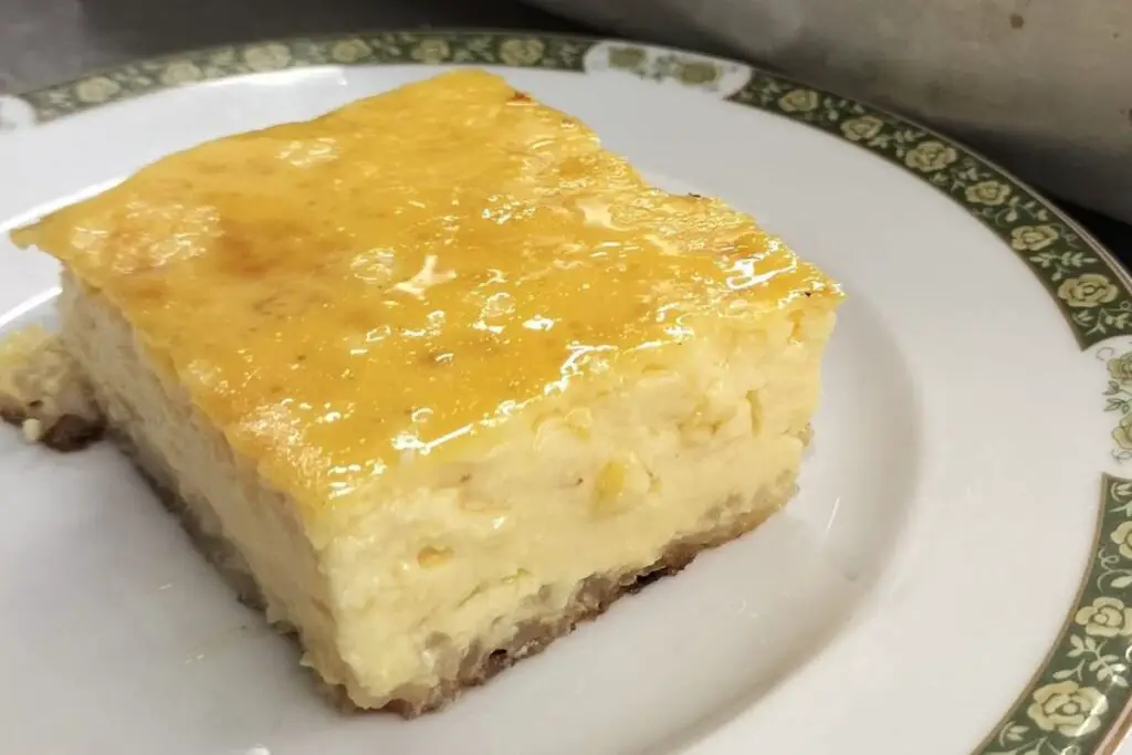 A square slice of Torta di riso, this rice cake has a very symmetrical and compact appearance, it is quite high and you can see the grains of rice inside while it is creamy and yellowish on top.