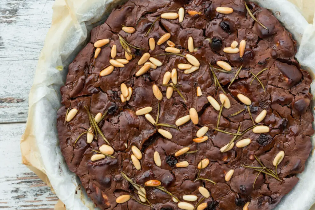 A typical Tuscan winter cake, the castagnaccio. Made only with chestnut flour, raisins, toasted pine nuts and rosemary can also be seen on the surface, although it is brown in color it does not contain chocolate.