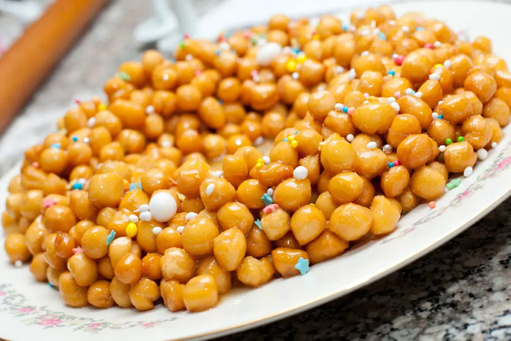 A tray full of struffoli, this typical Neapolitan sweet consists of many little yellow balls that form a mound, held together by honey. Their texture is crunchy on the outside, crumbly inside, and sticky