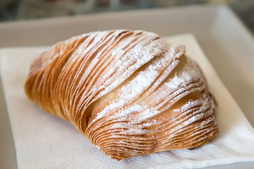 A Neapolitan sfogliatella, shaped like a shell with layers of pastry overlapping to form a crispy, golden-brown crust