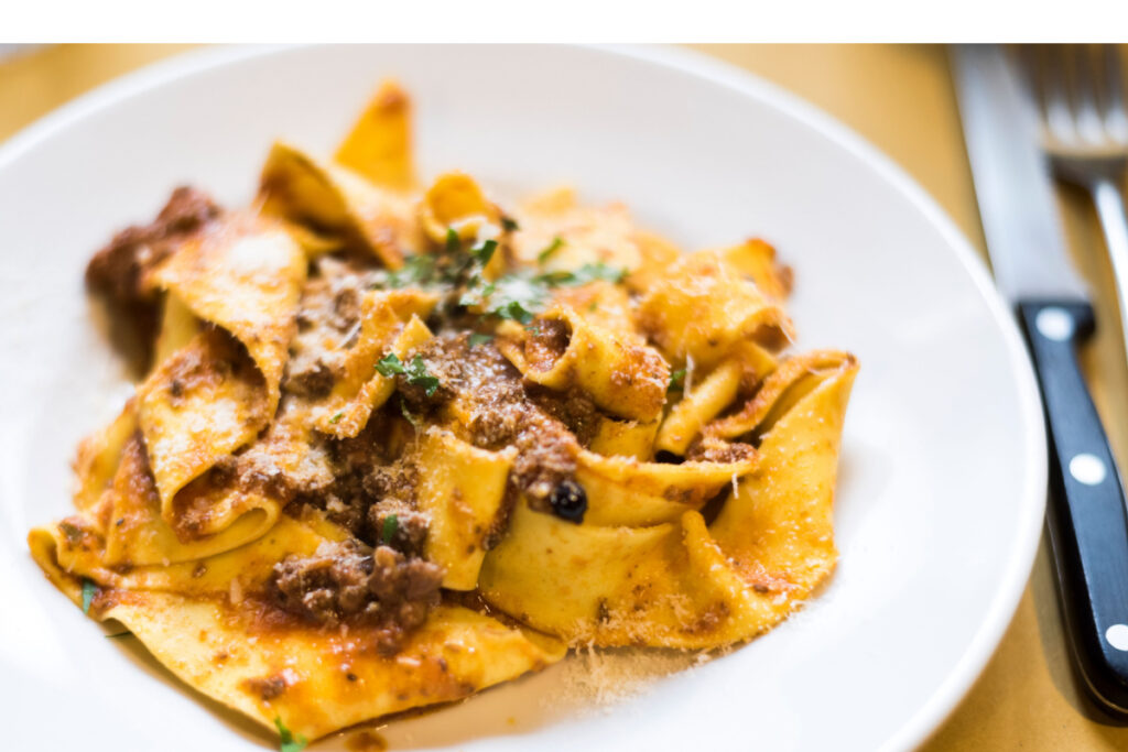 A plate of pappardelle, an egg pasta in the form of wide rectangular strips. Seasoned with a hare meat sauce, with a rustic appearance and a deep red colour.