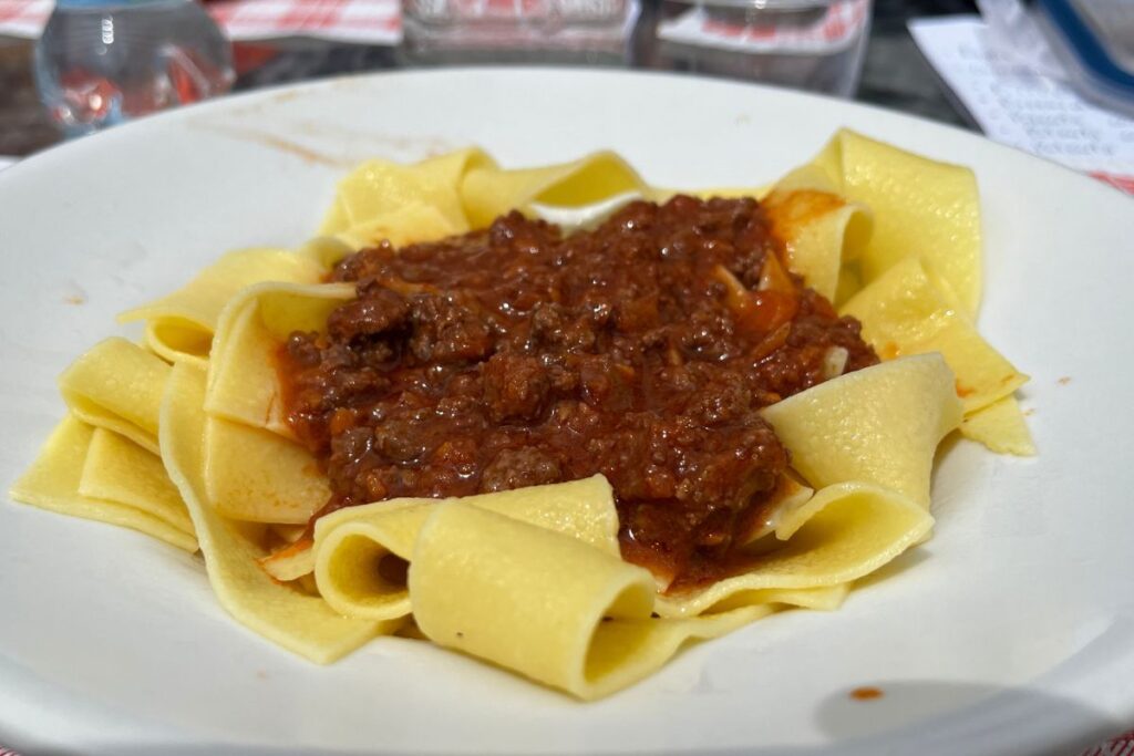 A plate of pappardelle, a pasta in the shape of large rectangular strips, seasoned with a deep red, almost bordeaux-colored wild boar sauce.