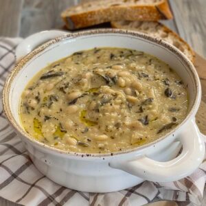 A thick soup of mashed beans, cannellini beans and black cabbage, the soup seems to have cooked for hours and is seasoned with a drizzle of oil. Next to the soup bowl is a slice of Tuscan bread.