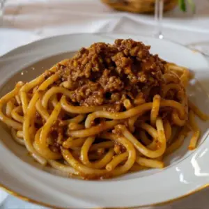 A close up of a dish with pici with Cinta Senese ragu, a handmade pasta shape that resembles thick irregular spaghetti, seasoned with a red ragù of pork loin and pork sausages.