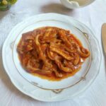 A dish of veal tripe cooked with a very rich and dense burgundy red tomato sauce, the tripe is cut into strips, it seems very tender and overcooked.
