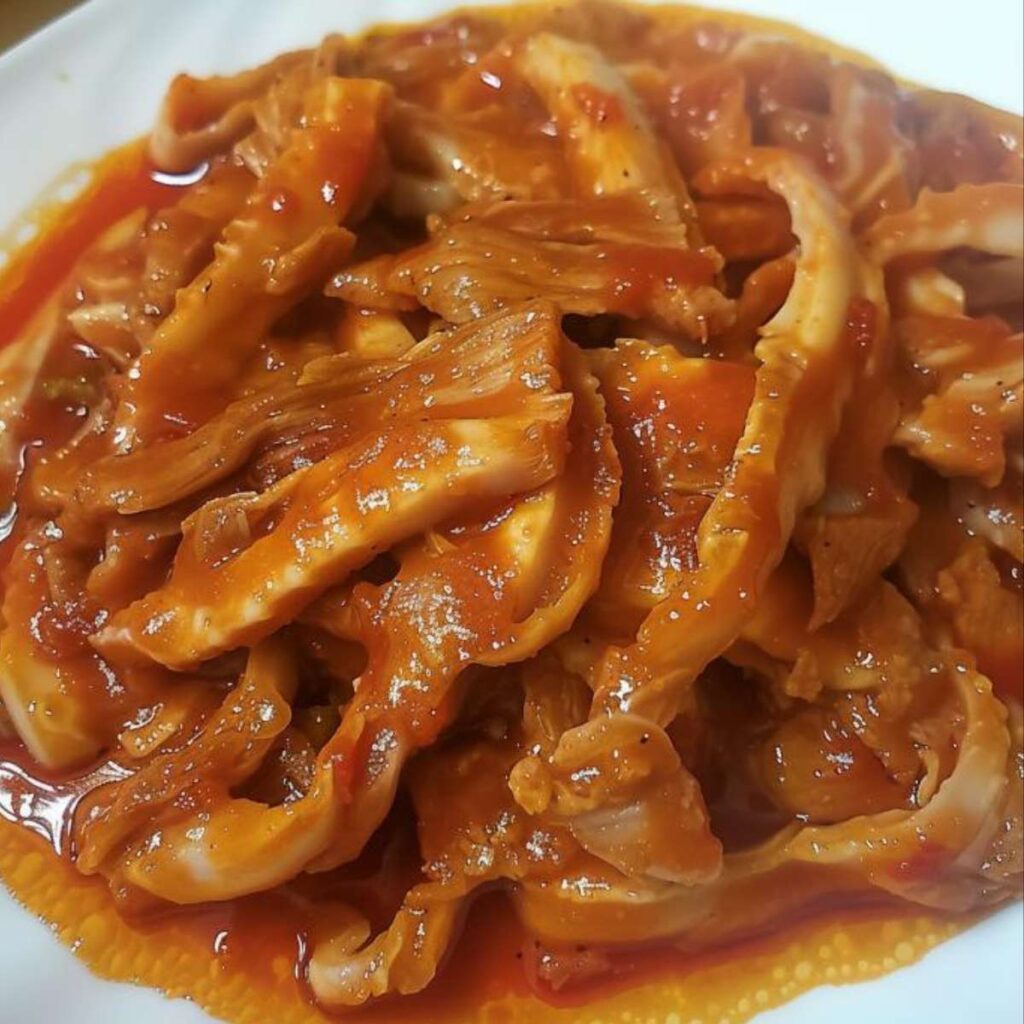 A close up of a dish of veal tripe cooked with a very rich and dense burgundy red tomato sauce, the tripe is cut into strips, it seems very tender and overcooked.