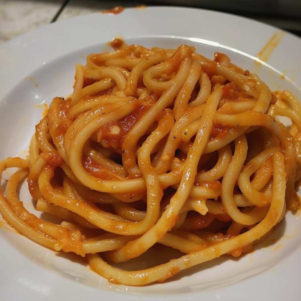 A type of pasta resembling very thick spaghetti, served with a tomato and garlic sauce, with a reddish-orange color.