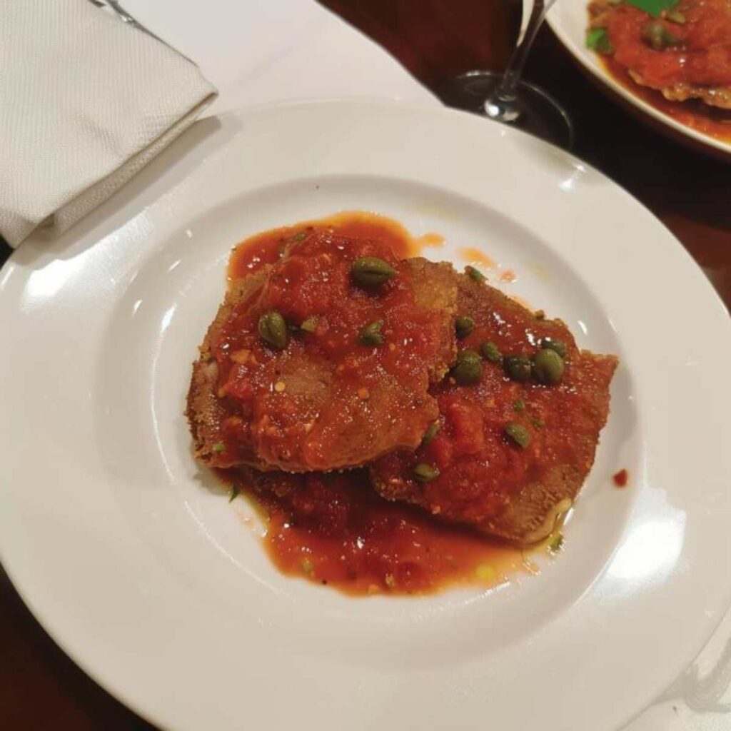Tender beef or veal slices smothered in a thick, flavorful tomato sauce, transforming their crunchy coating into a juicy delight. The sauce, enriched with capers, adds a tangy contrast to the savory meat, creating a perfect balance of rich and zesty.