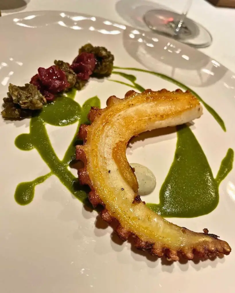 A perfectly grilled octopus leg served with vibrant green sauce and garnishes, highlighting the culinary excellence at Ventuno Bistrot, one of the best restaurants in Florence Italy.