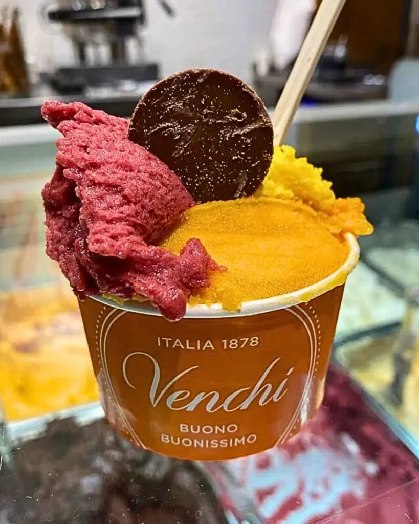 A cup of vibrant, creamy gelato from Venchi Cioccolato e Gelato, showcasing a variety of flavors in the background.