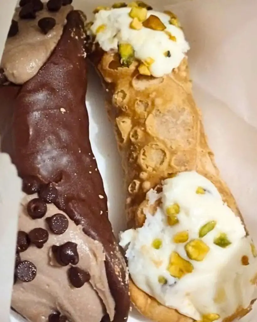 Italian dessert cannoli from Veniero's Pasticceria & Caffe, showcasing a mix of plain, chocolate-covered, and pistachio-studded cannoli.