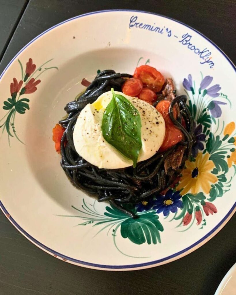 A plate of squid ink pasta topped with cherry tomatoes and burrata at Cremini's in Brooklyn, a top-rated Italian restaurant in NYC.