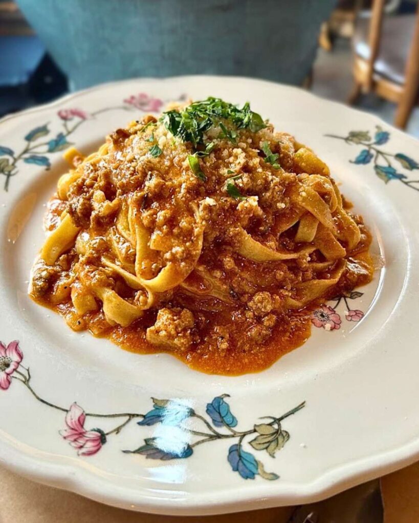 Fresh pasta topped with a rich meat sauce, garnished with herbs, served on a decorative plate at Al Di La Trattoria in NYC.