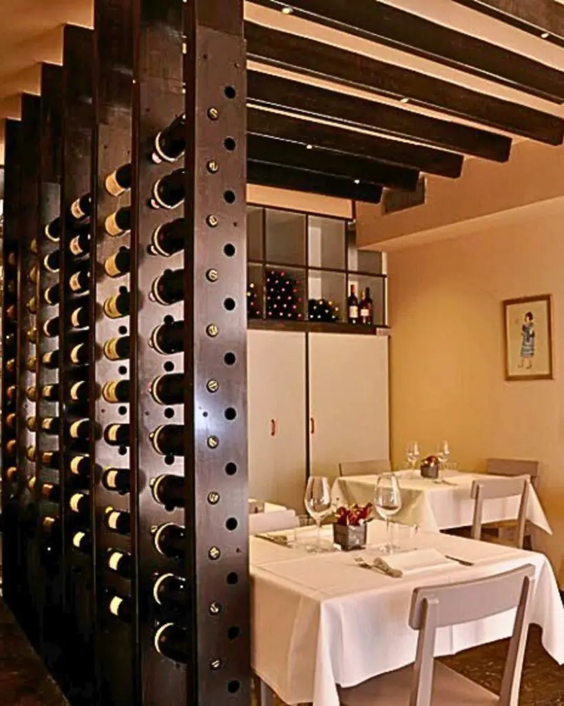 An elegant dining setting at La Bottega di Parigi in Florence, featuring a modern wine rack filled with selections of fine wines, paired with pristine white tablecloths and simple yet stylish decor that enhances the intimate and sophisticated ambiance.