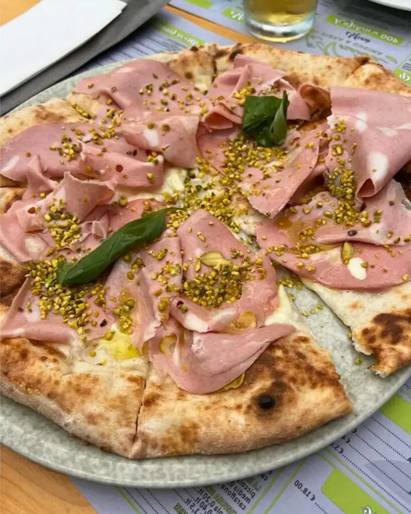 Close-up of a pizza topped with slices of mortadella, pistachios, and basil leaves at La Veranda Siena.