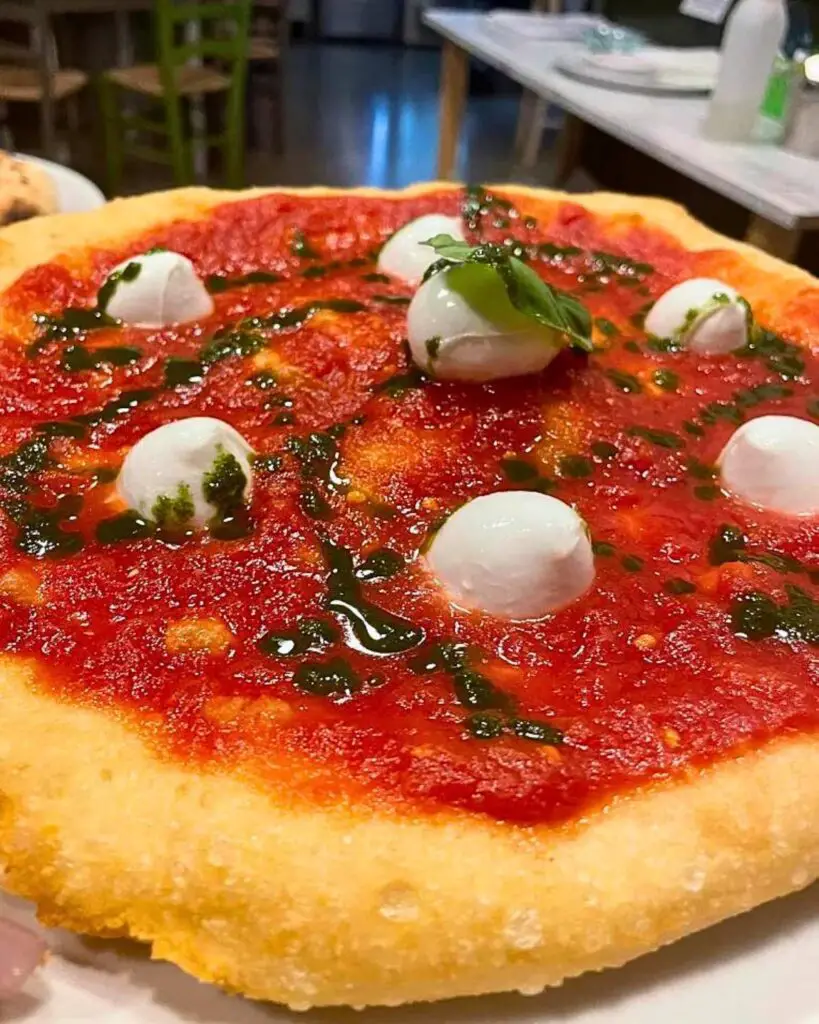 Close-up of a pizza topped with fresh tomato sauce, mini mozzarella balls, and basil leaves at La Bella 'Mbriana 2.0