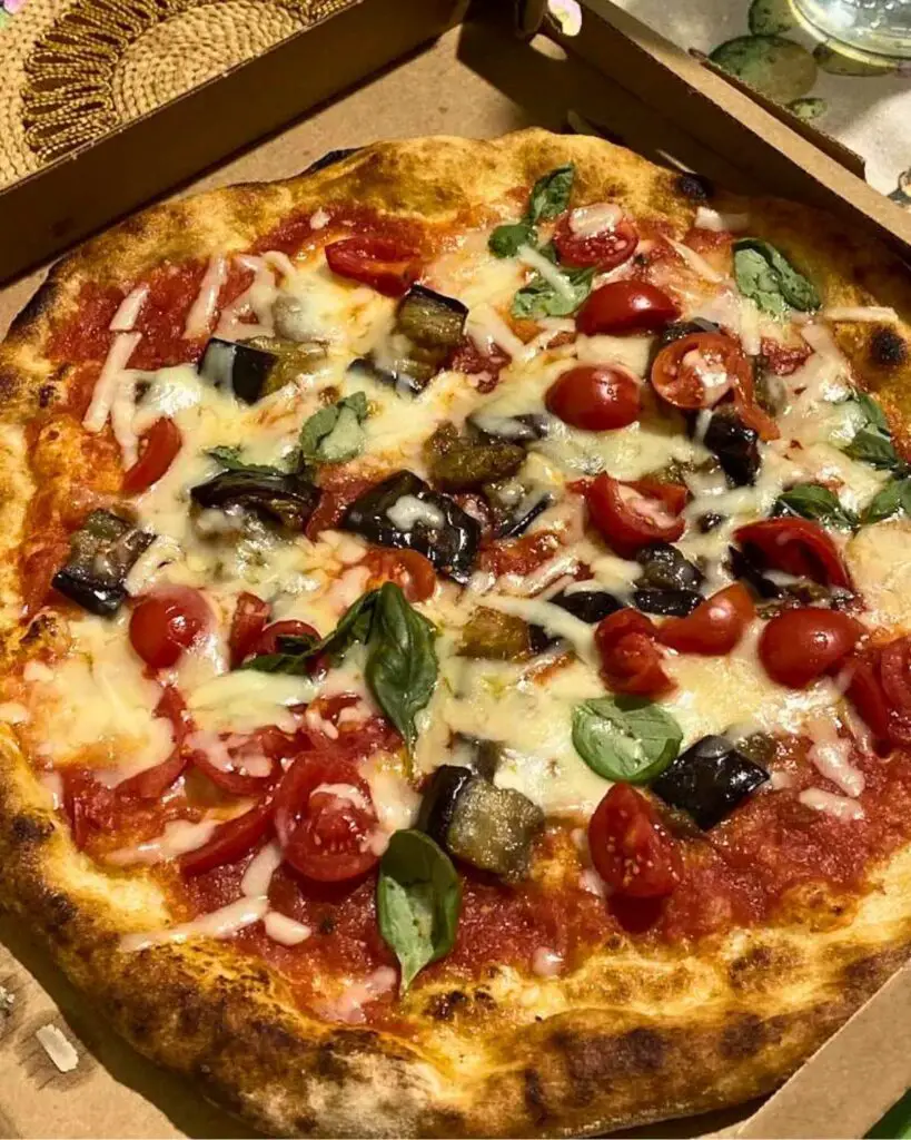 A close-up of a delicious pizza topped with cherry tomatoes, eggplant, and fresh basil at Pizzeria Alle Scalette in Siena.