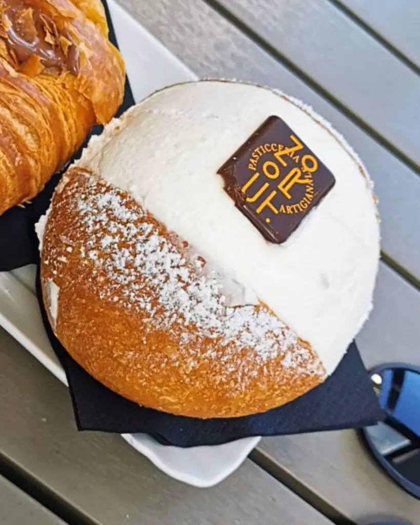 Famous maritozzo from CON.TRO pastry shop in Rome, topped with fresh whipped cream and a chocolate logo.