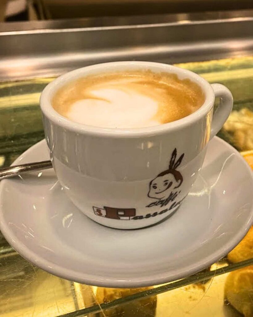 A creamy cappuccino served in a white cup with the logo of Augustus Napoli, highlighting the Naples Italy coffee and coffee in Italy experience.