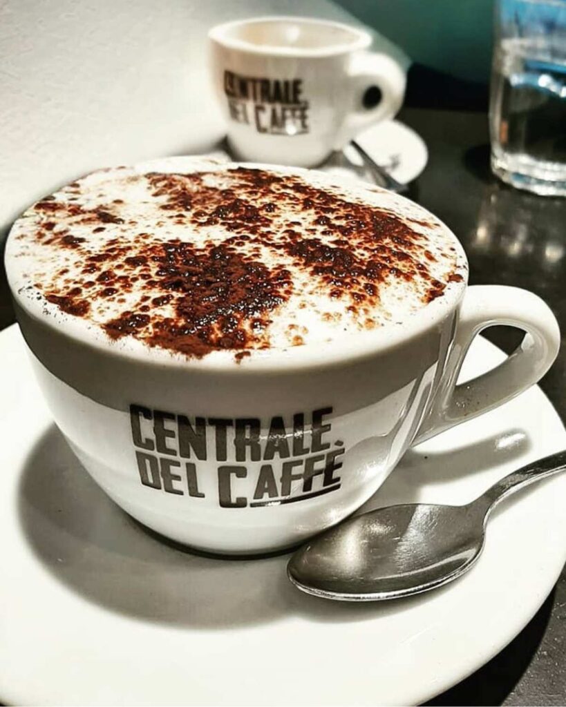 A cappuccino with cocoa powder in a white cup labeled "Centrale Del Caffè," showcasing the coffee in Naples and unique cafe experience.